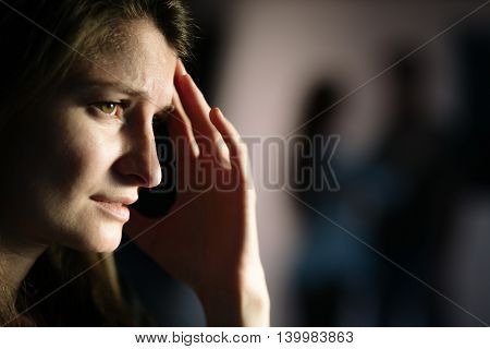 Sad young woman is suffering after breakup while having flashbacks with her boyfriend - couple silhouettes on the background