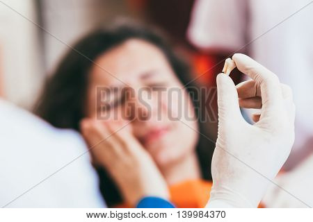 Blurry pose of a woman with toothache and a dentist hand holding the extracted tooth. Focus on the hand