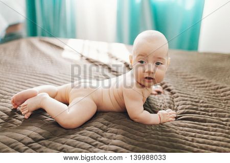 Closeup of an adorable naked baby boy lying in bed and looking away
