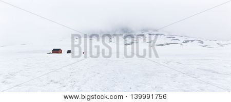 Panoramic Winter view on the Classic Red Hut (rorbu) in the mountain peak  White cloud. Near The Snow Road, Norway - Aurlandsfjellet National Tourist Route