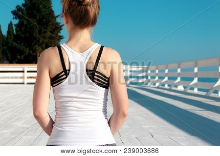 Young Slim Woman In Tight Sportswear Practicing Yoga Outdoors At White Wooden Seafront. Back View Ei