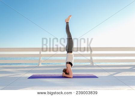 Young Slim Woman In Tight Sportswear Practicing Yoga Outdoors At White Wooden Seafront.