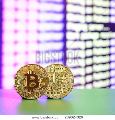 Two Gold Bitcoins Lie On The Green Surface On The Background Of The Display, Which Shows The Process