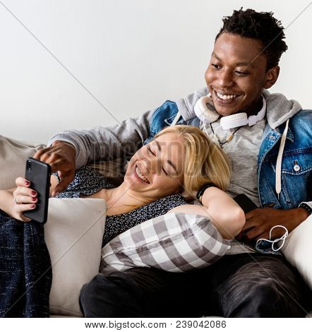 Cute interracial couple on a couch sharing smartphone love, internet and music concept