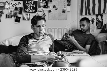 Teenage boys hanging out in a bedroom playing a video game and using a smartphone