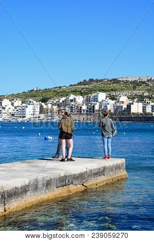 San Pawl, Malta - April 2, 2017 - Three Young People Standing On A Small Jetty With Views Towards St