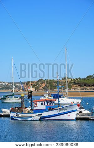 Alvor, Portugal - June 7, 2017 - Fishing Boat Moored Against A Jetty In The Estuary With Yachts To T