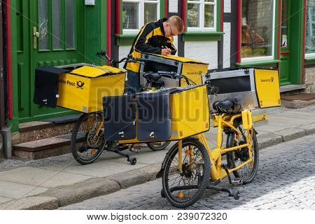 Wernigerode, Germany - April 26, 2018: German Postman Of The Deutsche Post Delivering Mail Using An 
