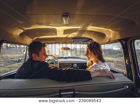 Young Wedding Couple Sitting Smiling Inside Retro Car And Looking At Each Other. Just Married Embrac