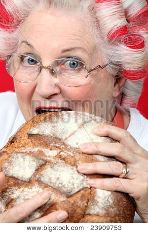 En gammel dame med hairroller på, bidende på et brød.