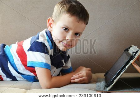 Little Cute Boy In T-shirt Playing Games On A Tablet And Watching Cartoons. Toddler With Tablet. At 