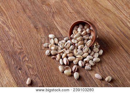 Overturned Ceramic Bowl With Pistachios On Wooden Background, Top View, Selective Focus. Some Copy S