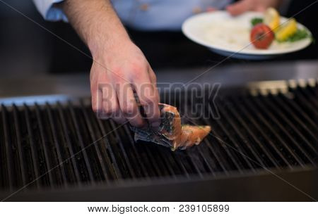Master chef hands cooking grilled salmon fish with potatoes on a restaurant kitchen