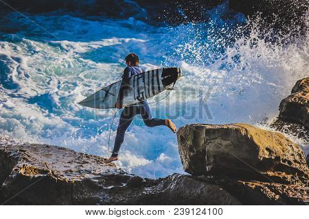Male Surfer Running Down The Rocky Shores With Waves Crashing Against The Rocks, Laguna Beach, Calif