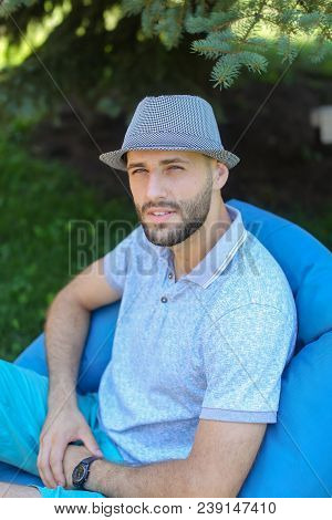 Man Sitting In Bag Chair Outside And Wearing Blue Hat. Concept Of Vacations And Resting In Open Air.
