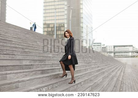 European Businesswoman Going Up On Stairs In High Buildings Background. Concept Of Career And Busine