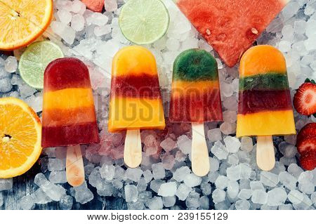 high angle view of some different homemade ice pops, made with different natural fruit juices and pieces of fruit, such as watermelon, strawberry, peach, lime or orange, placed on ice