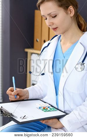 Woman Doctor Write Prescription While Sitting In Hospital Office. A Lot Of Various Colored Pills Liy