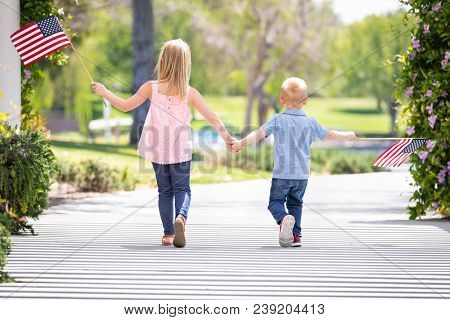 Young Sister and Brother Holding Hands and Waving American Flags At The Park.