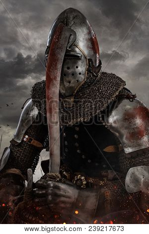 Knight With Sword In Battlefield With Dark Clouds On Background.