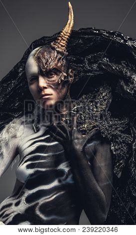Portrait Of Devil Woman In Black And White Clothes With One Horn On Her Head. Isolated On Grey Backg