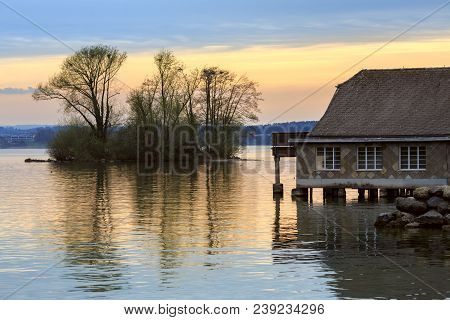 View Of The Lake Zug In The Spring During Sunset. Old Residential House Built On Water. Town Of Cham