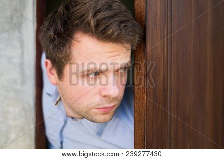 Young Caucasian Man With Agoraphobia Spying And Looking Out The Door. He Is Afraid Of Communication 