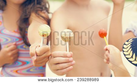 Cute Brother And Sisters Enjoying Their Lollipops Outside At The Beach.