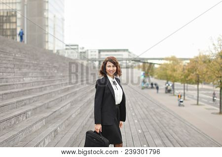 Female Caucasian Secretary Standing On Stairs With Bag And High Buildings In Background. Concept Of 