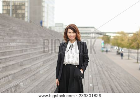 Pretty European Female Manager Standing On Stairs Outside In High Buildings Background. Concept Of P