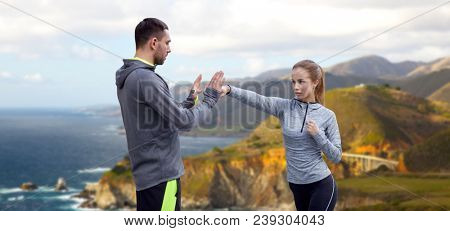 fitness, sport, martial arts and people concept - happy woman with personal trainer working on strike over bixby creek bridge on big sur coast of california background