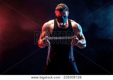 Portrait Of Muscular Sportsman In Training Mask Tearing Metal Chain.black Background With Blue, Red 