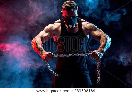 Portrait Of Muscular Sportsman In Training Mask Tearing Metal Chain.black Background With Blue, Red 
