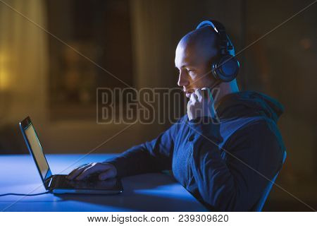 cybercrime, hacking and technology concept - male hacker with headset using laptop computer for cyber attack or wiretapping in dark room