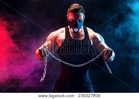 Portrait Of Muscular Sportsman In Training Mask Tearing Metal Chain.black Background With Blue, Red 