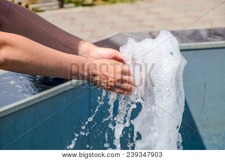 Hand Touch The Fountain. A Stream Of Water From The Fountain Is Touched By Hand.