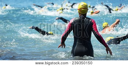 Group Triathlon Participants Running Into The Water For Swim Portion Of Race,splash Of Water And Ath