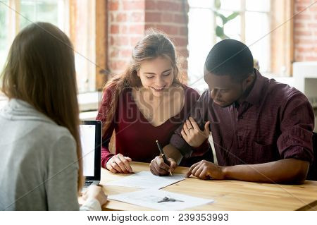 Smiling Wife Watching African American Husband Signing Purchase Deal From Female Real Estate Agent. 
