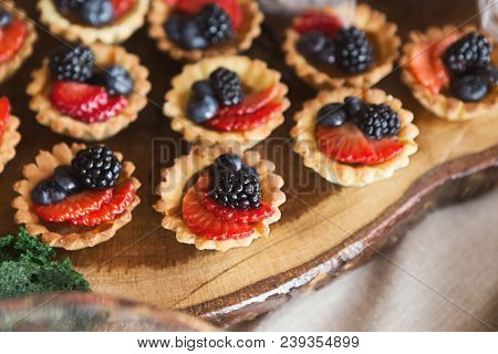 Closeup Of Berry Mini Tarts On Wooden Board. Small Tartalettes For Party Dessert Stand. Candy Bar An