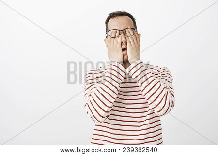 Portrait Of Exhausted Uncomfortable Male Model In Striped Pullover And Glasses, Rubbing Eyes, Feelin