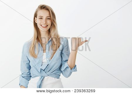 Portrait Of Positive Good-looking European Girl With Blond Hair In Stylish Shirt, Raising Hand And P