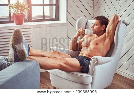 Handsome Shirtless Muscular Man Lying On The Chair, Drink Cup Of Tea, Resting After A Hard Workout A