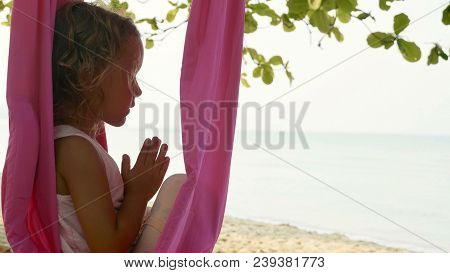 Little Cute Child Girl Doing Yoga Exersice With Namaskar Gesture Hammock In The Beach.