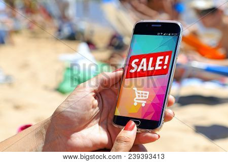 Girl On The Beach Holding A Smartphone A Sale Advertising On The Screen. Marketing, Discount, Intern