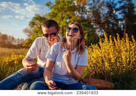 Happy Young Couple Hanging In Their Phones And Laughing Outside. Woman And Man Relaing After Having 
