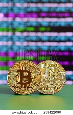 Two Gold Bitcoins Lie On The Green Surface On The Background Of The Display, Which Shows The Process