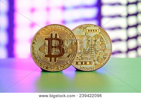 Two Gold Bitcoins Lie On The Green Surface On The Background Of The Display, Which Shows The Process