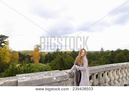 Young Caucasian Female Person Standing Near Concrete Railing With Green Trees Background. Concept Of