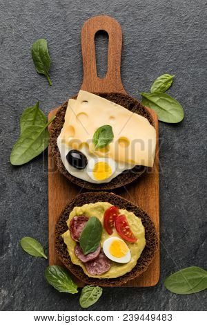 Open faced sausage sandwich canape or crostini on a wooden serving board  on dark stone background closeup. Top view.