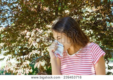 Allergy Concept. Sneezing Young Girl With Nose Wiper Among Blooming Trees In Park.